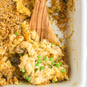 A wooden spoon scooping gluten-free tuna casserole from the baking dish