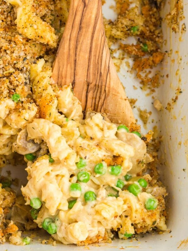 A wooden spoon scooping gluten-free tuna casserole from the baking dish