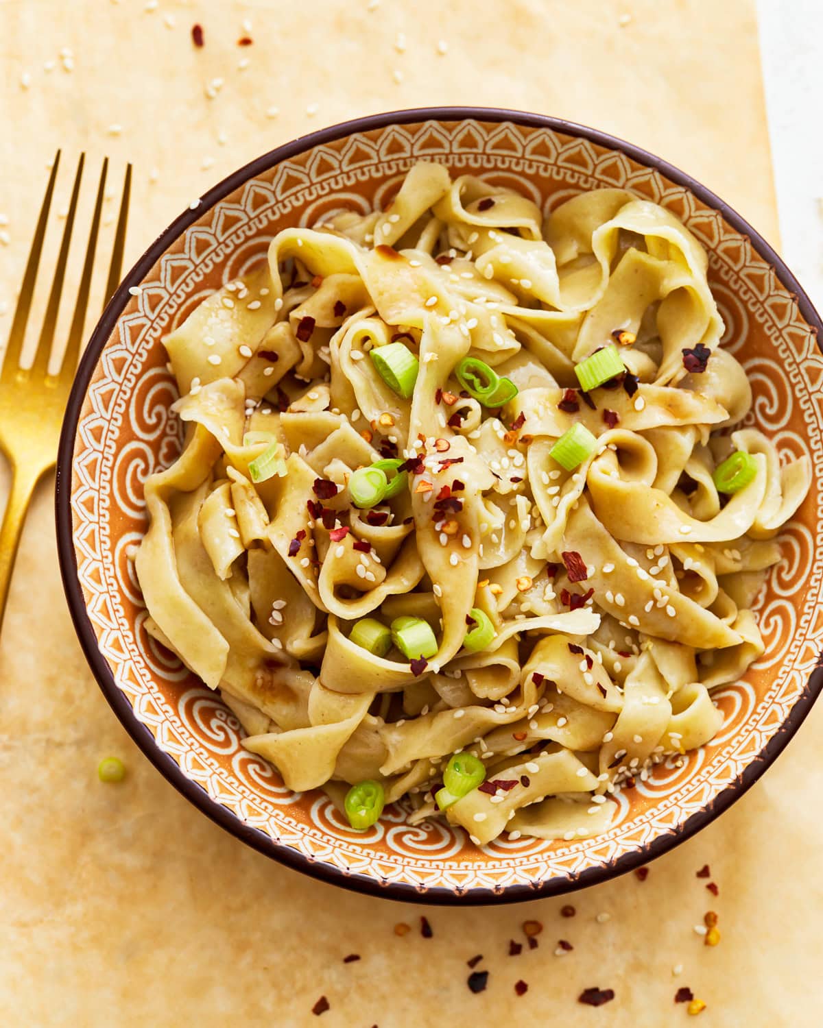 Gluten-free egg noodles in a bowl with green onions, sesame seeds, and red pepper flakes