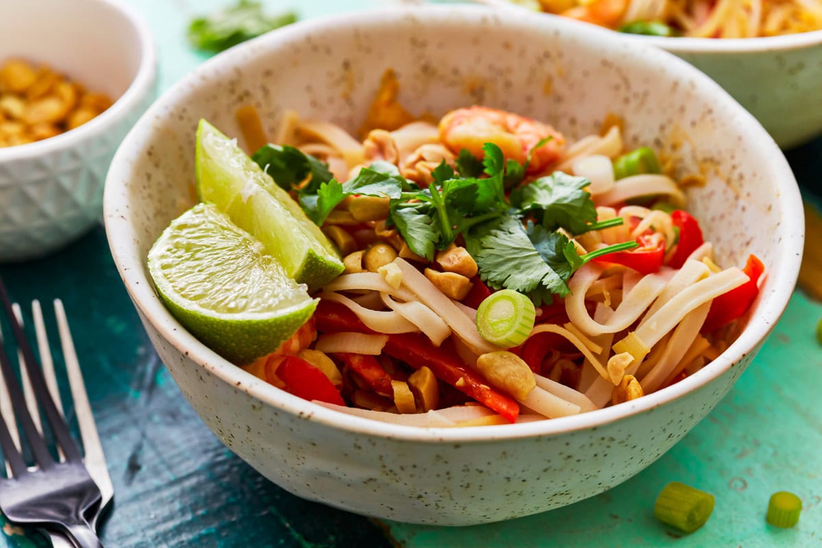 Gluten-free pad thai topped with cilantro, green onions, and lime wedges