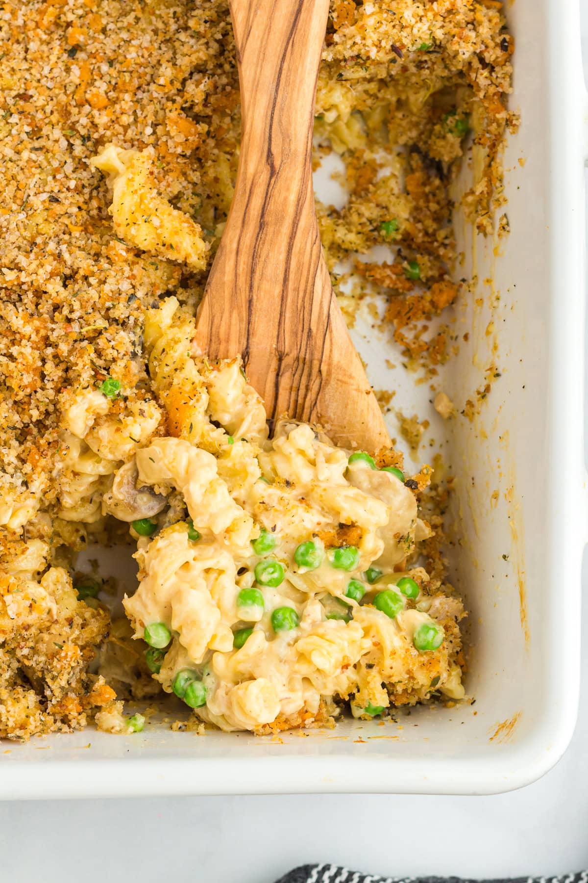 A wooden spoon scooping gluten-free tuna casserole from the baking dish