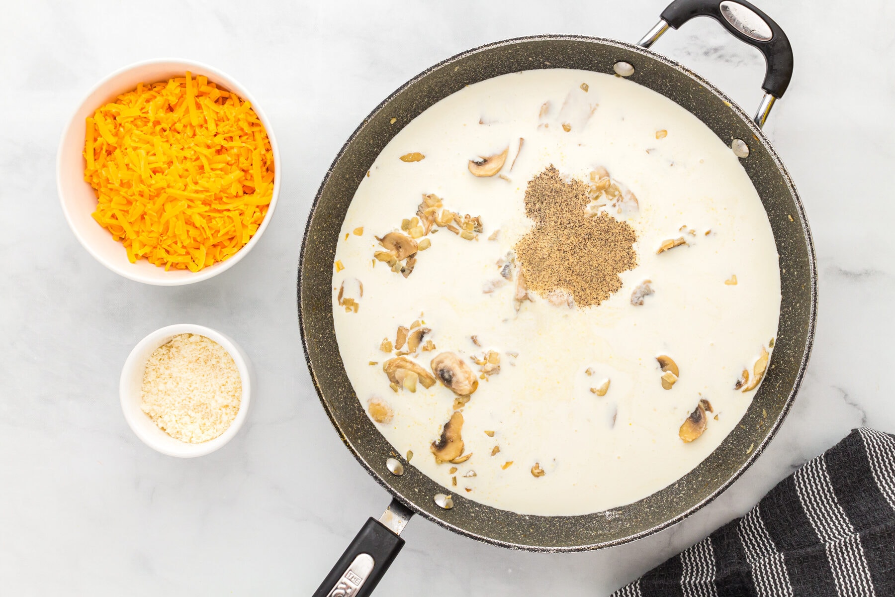 Seasonings, heavy cream, and chicken broth added to a skillet with mushrooms