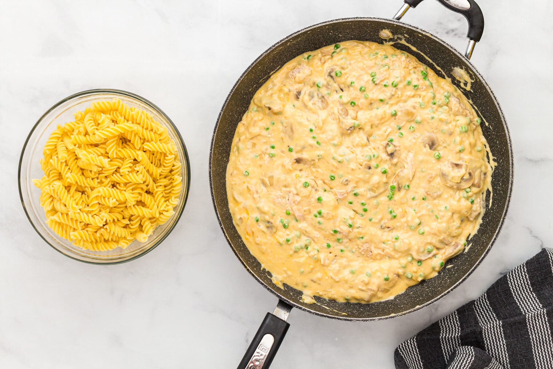 Tuna and peas added to the sauce for gluten-free tuna casserole in a skillet 