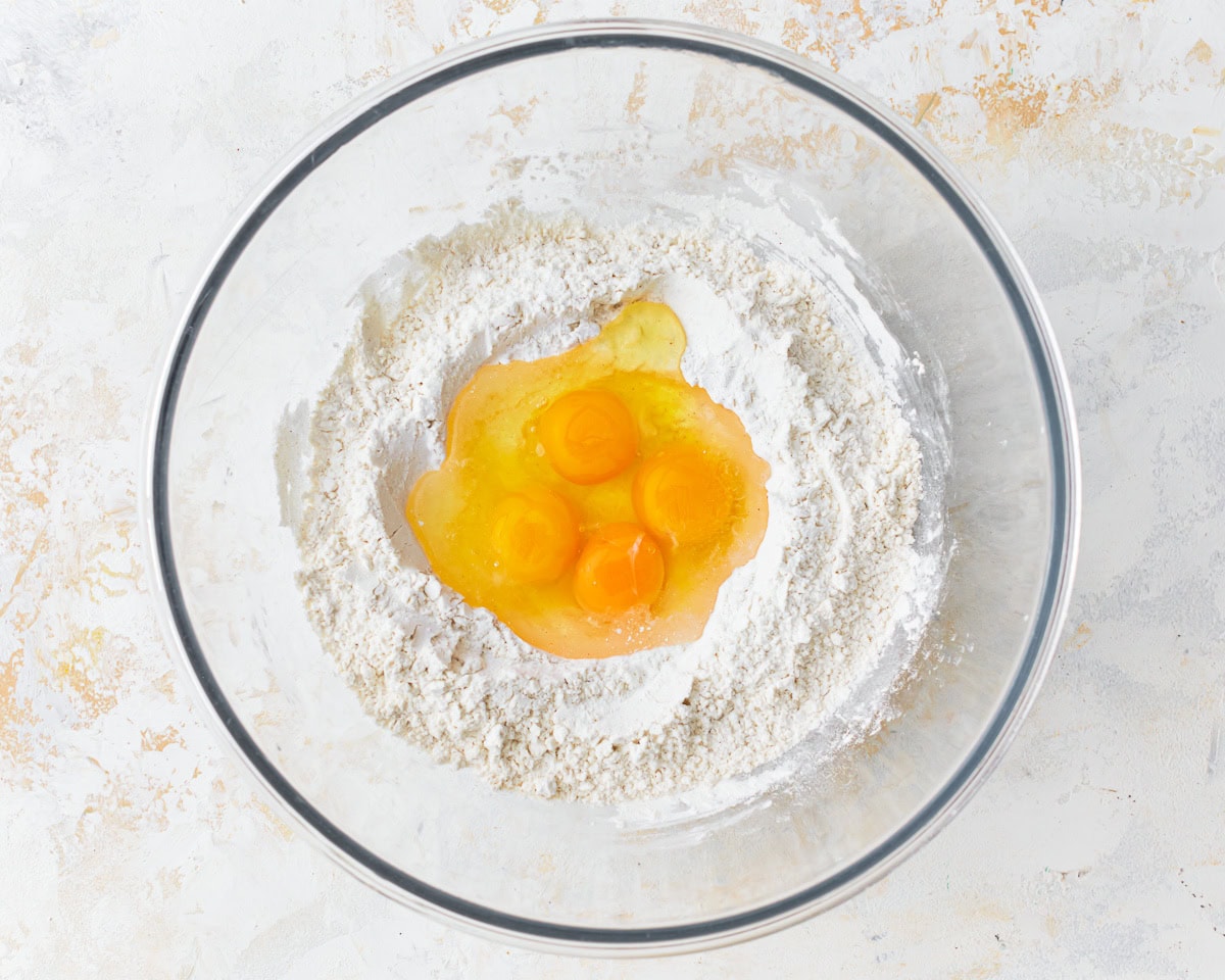 Eggs added to the dry ingredients for gluten-free noodles in a glass mixing bowl