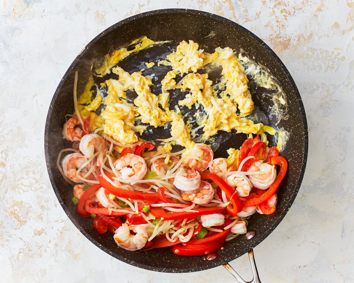 Eggs cooking in skillet with vegetables and shrimp for gluten-free pad thai