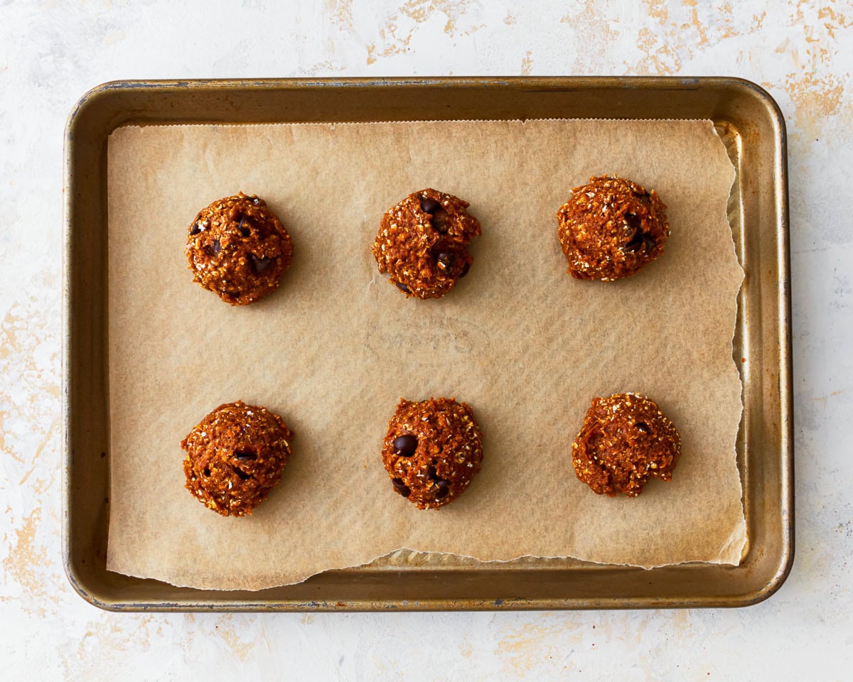 Scoops of gluten-free peanut butter oatmeal cookie dough on a parchment lined baking sheet