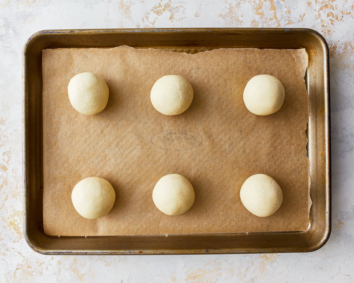 Balls of pandebono bread dough on a parchment lined baking sheet