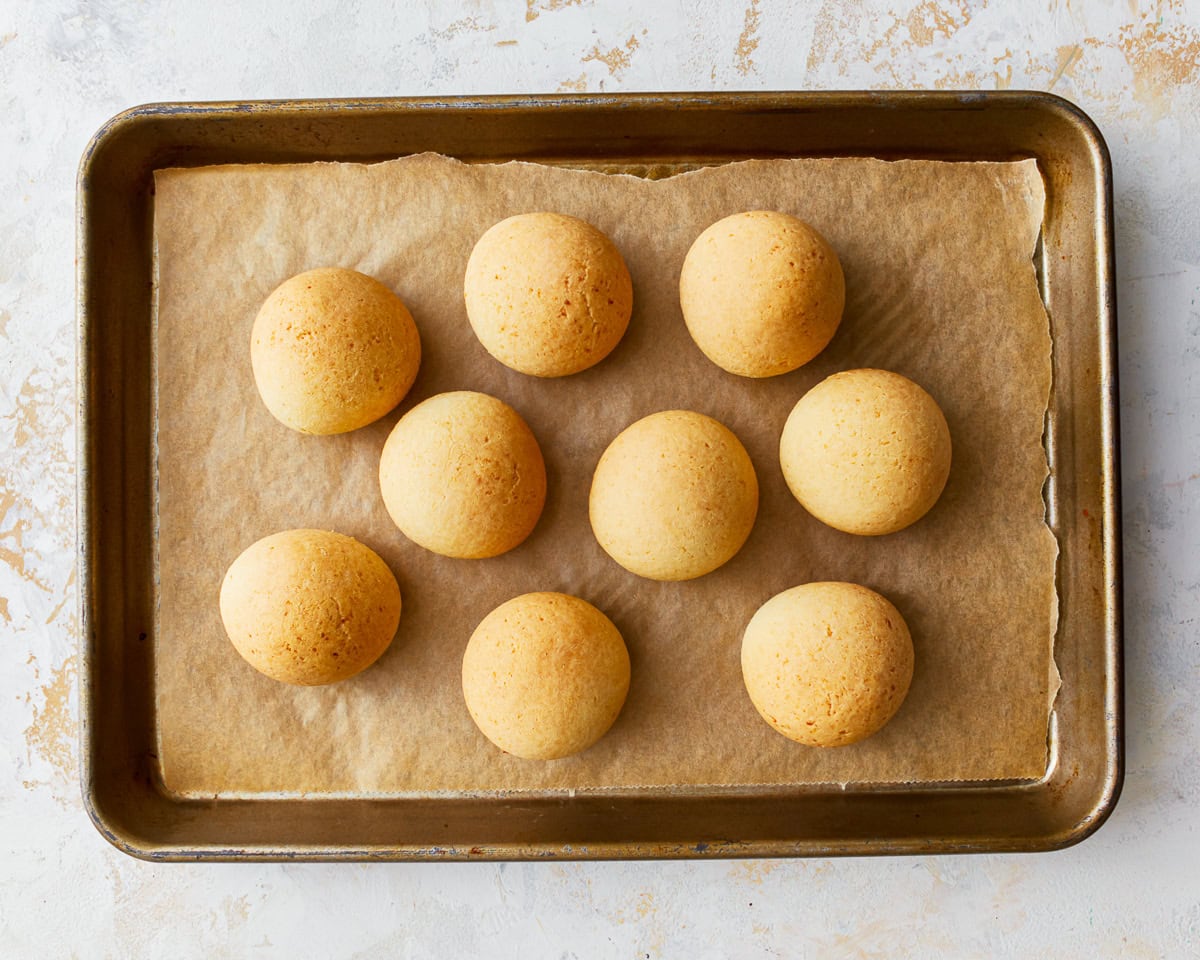 Freshly baked pandebono on a parchment lined baking sheet