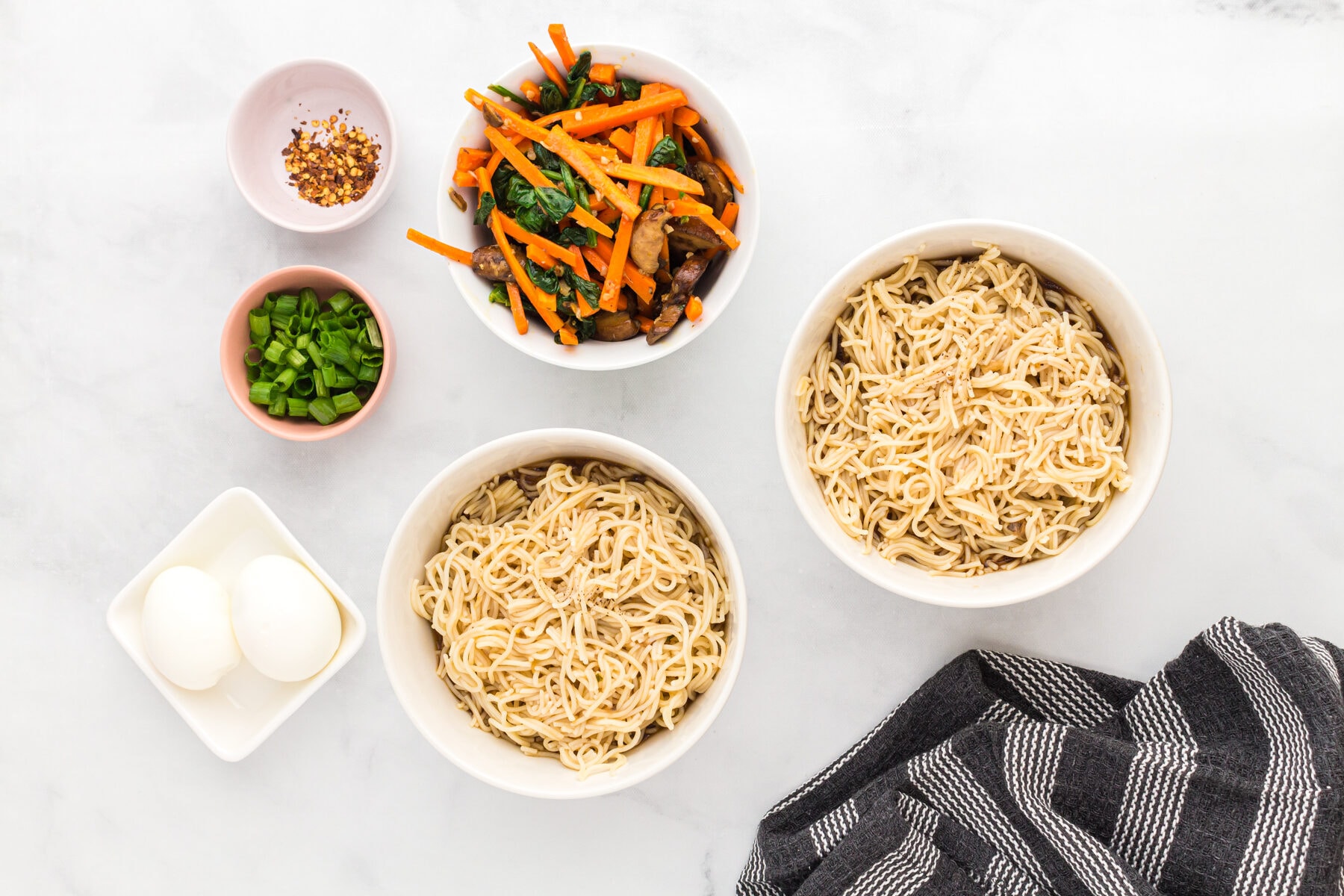 Gluten-free ramen noodles next to bowls of vegetables, green onions, and crushed red pepper flakes