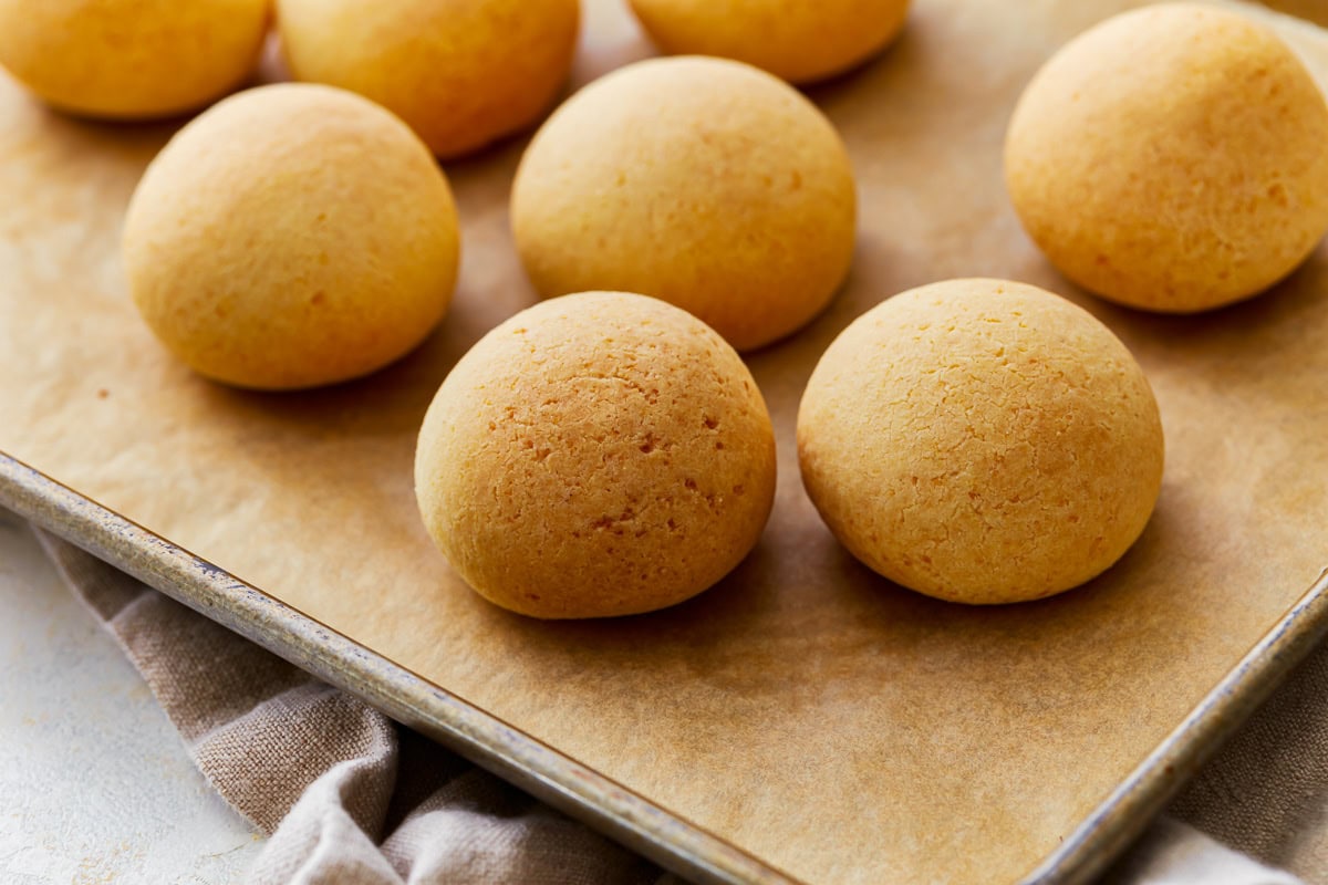 Side view of pandebono Colombian cheese bread on a parchment lined baking sheet