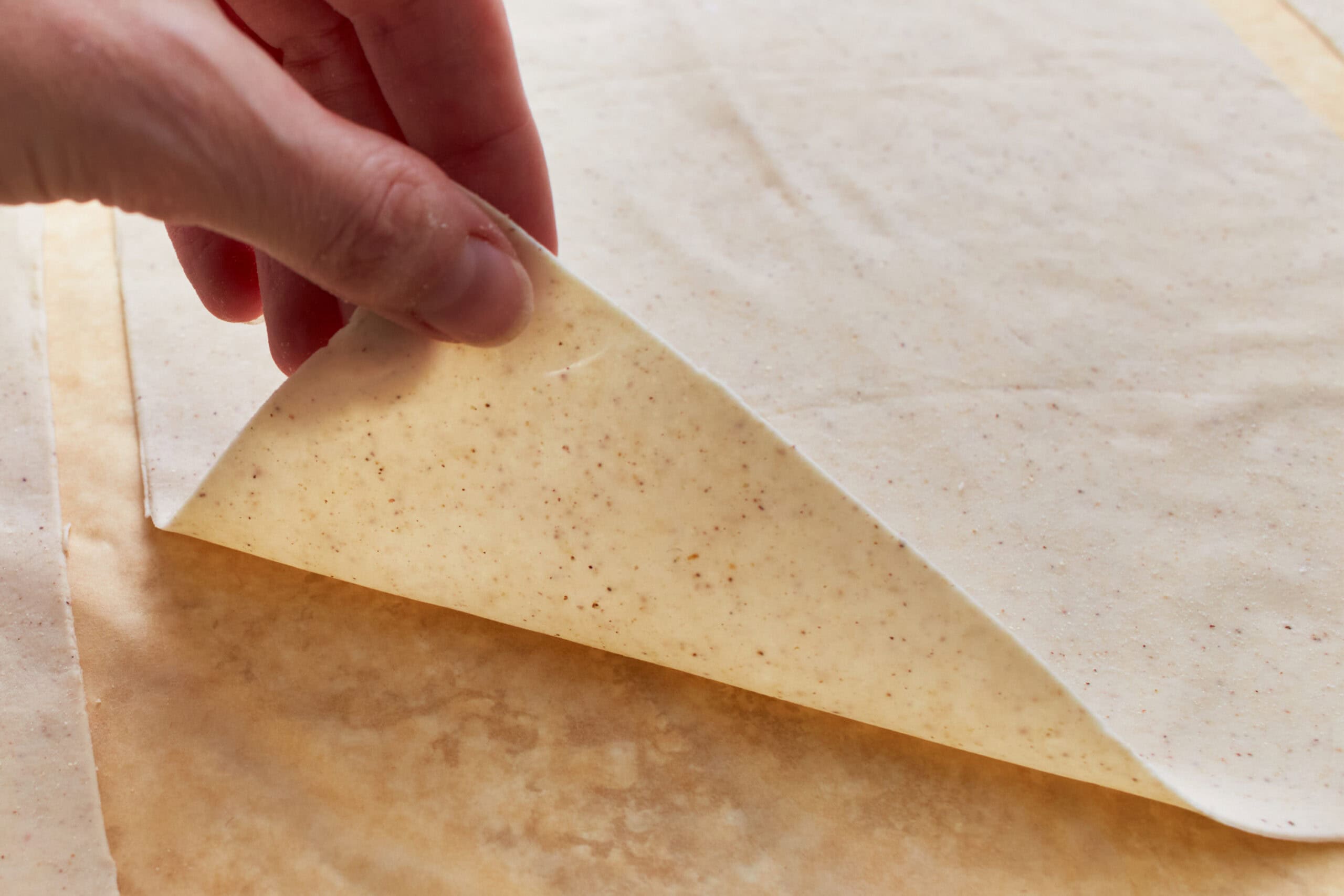 A hand lifting the corner of a piece of gluten-free phyllo dough.