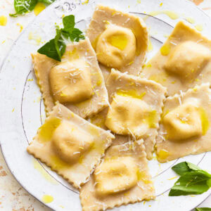 Gluten-free ravioli on a plate with fresh herbs and shredded cheese.