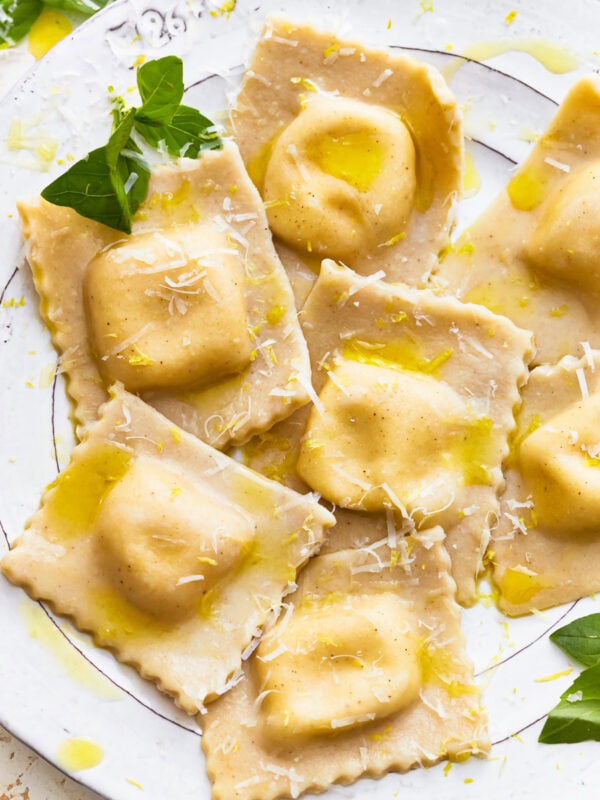 Gluten-free ravioli on a plate with fresh herbs and shredded cheese.