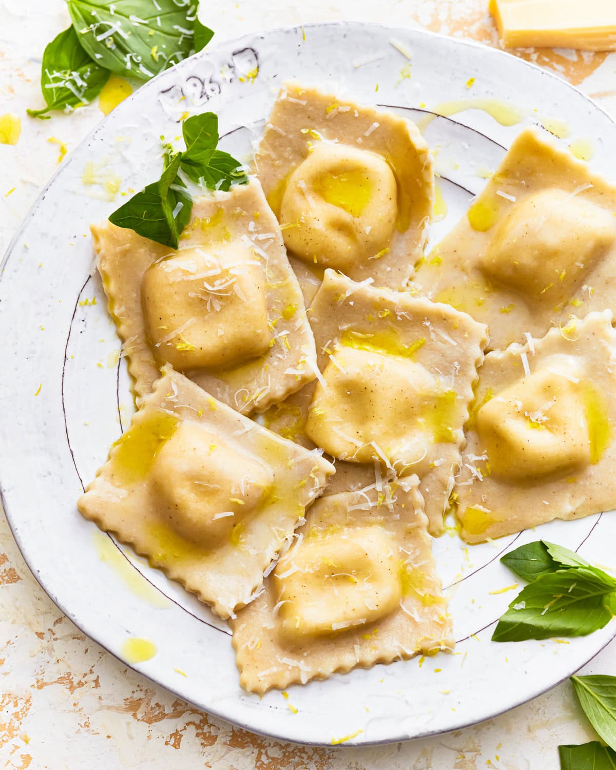 Gluten-free ravioli on a plate with fresh herbs, olive oil, and shredded cheese.