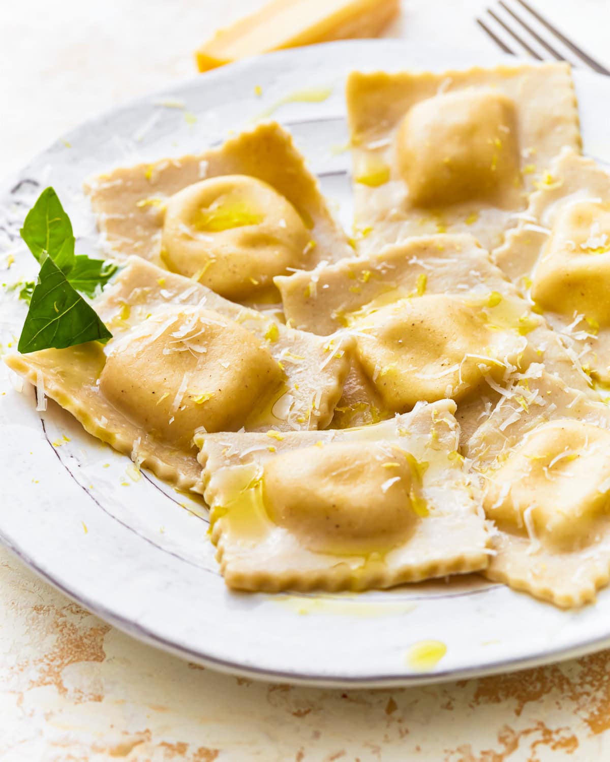 Side view of gluten-free ravioli on a plate with fresh herbs, olive oil, and shredded cheese.