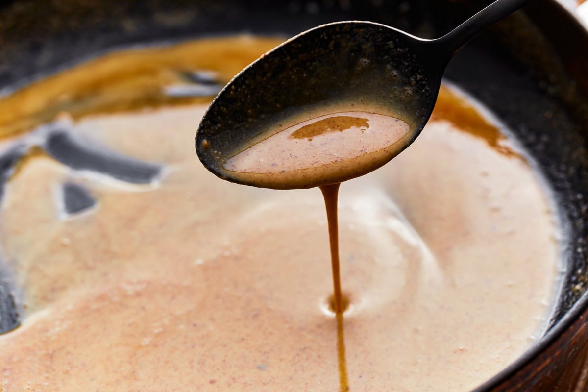 A spoon scooping gluten-free roux from a skillet.