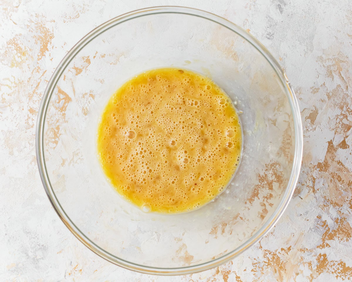 Beaten eggs in a glass mixing bowl.