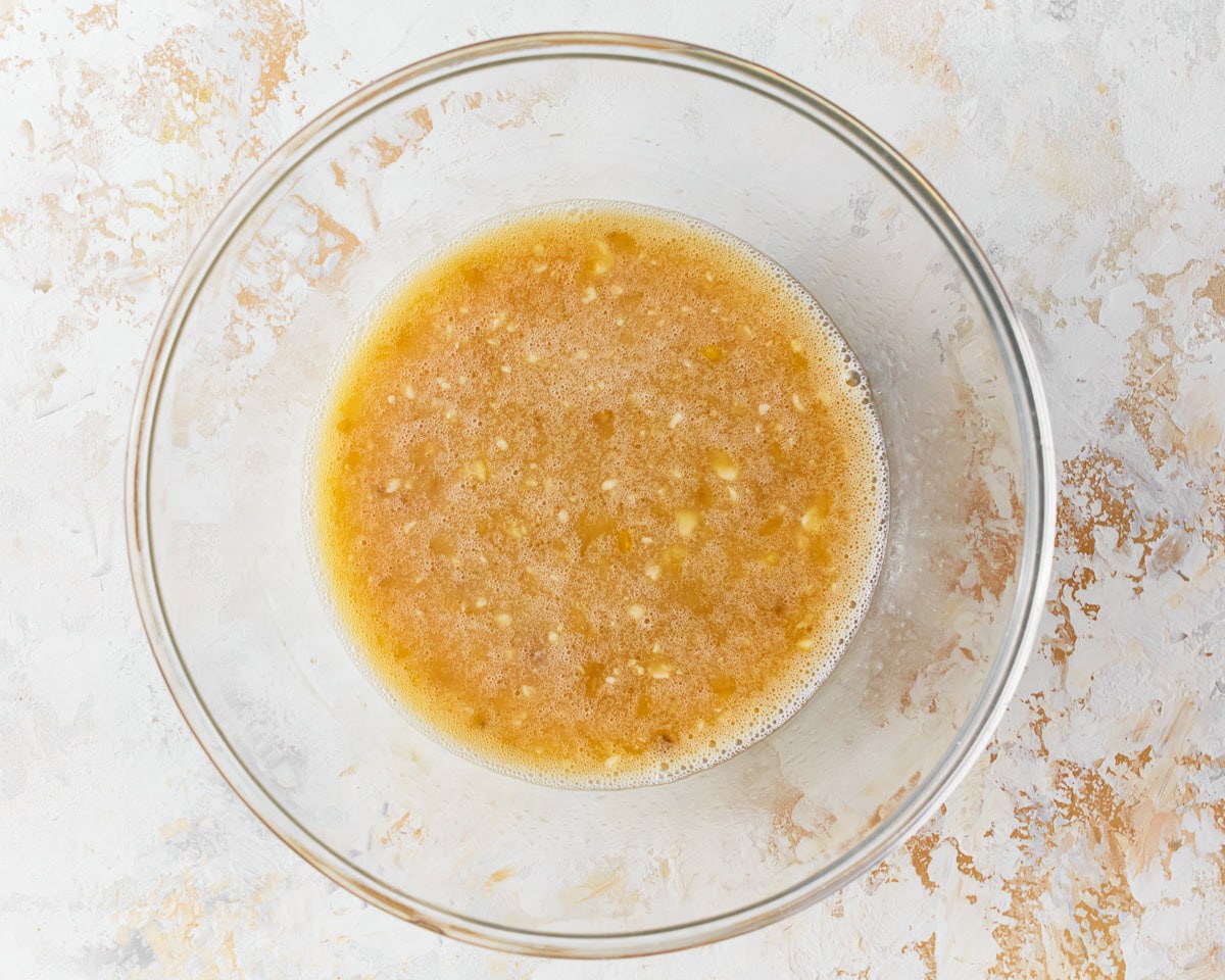 Mashed banana, coconut milk and oil, and honey added to a glass mixing bowl.