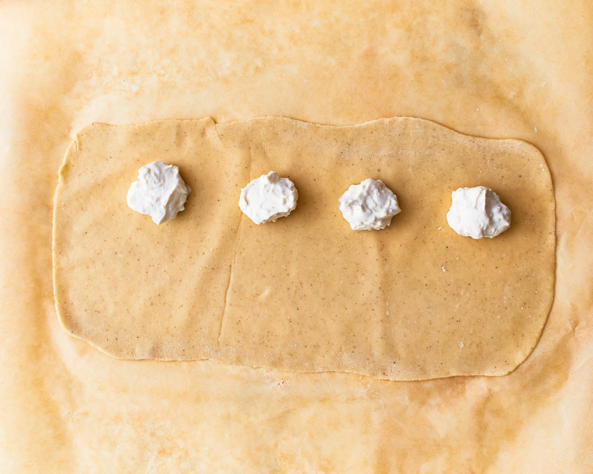 Spoonfuls of gluten-free ravioli filling on top of rolled out pasta dough.