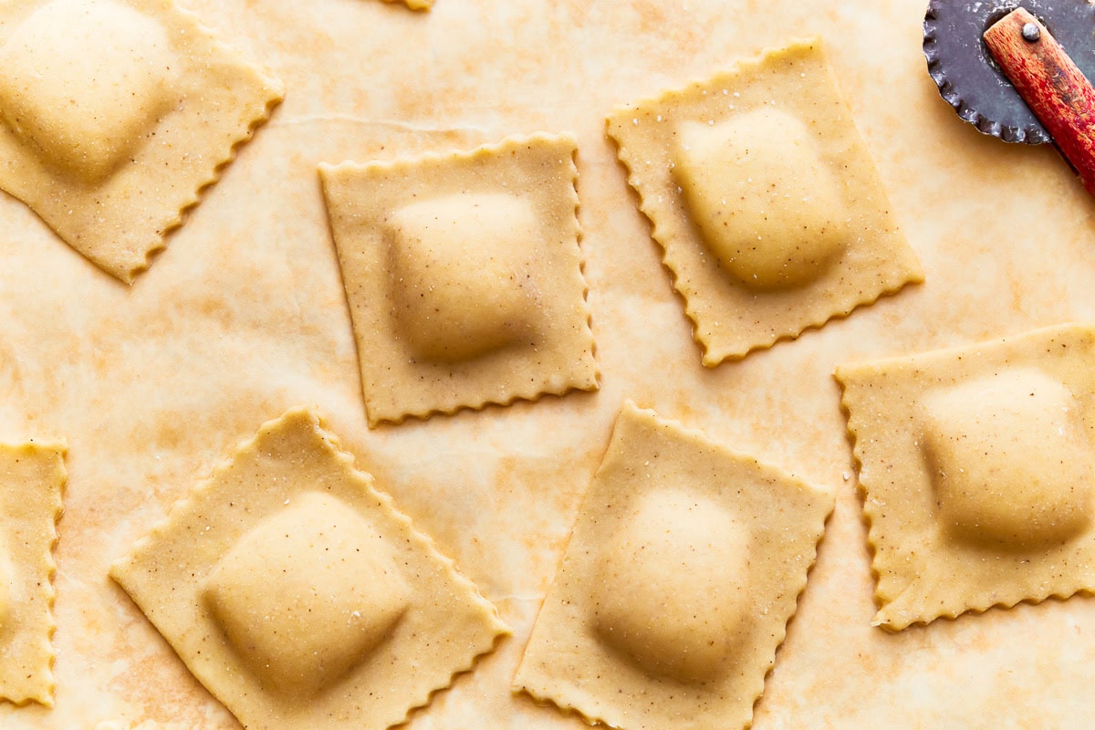 Shaped and filled gluten-free ravioli squares on parchment paper.