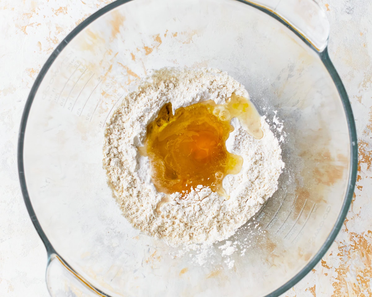 Eggs added to dry ingredients for gluten-free ravioli in a glass mixing bowl.