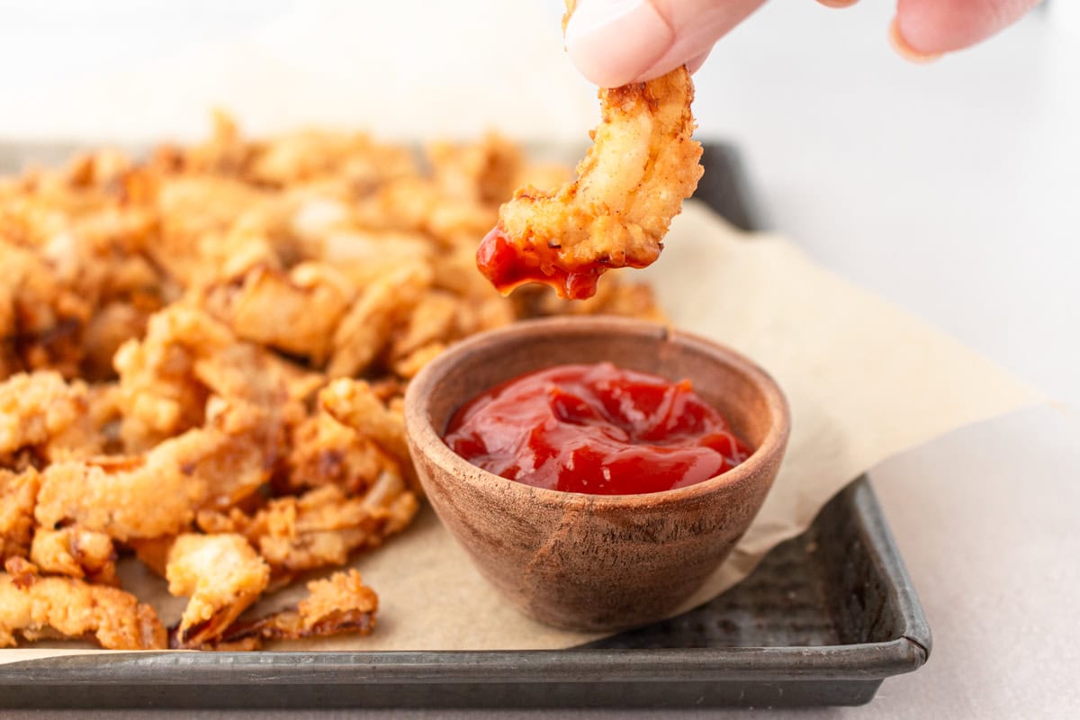 A tray of gluten-free fried onions with one dipped into tomato sauce.