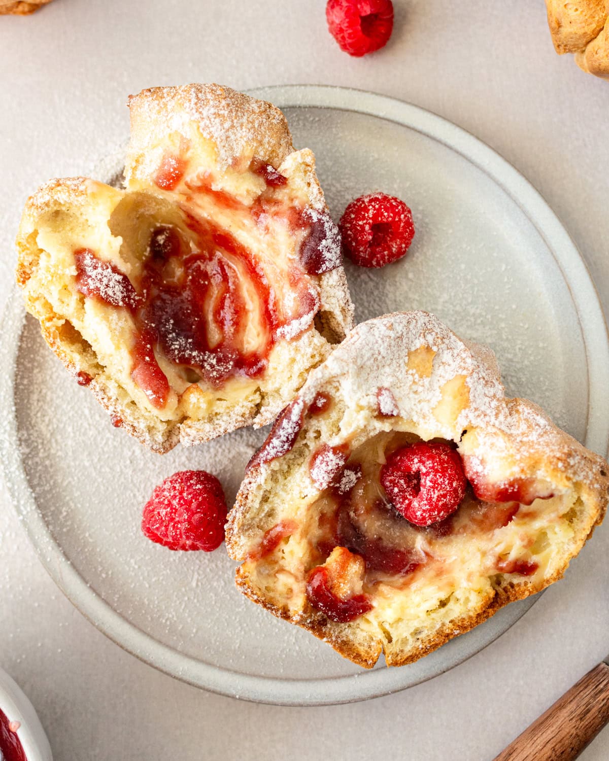 Overhead view of a gluten-free popover cut in half with raspberries and powdered sugar on a white plate.