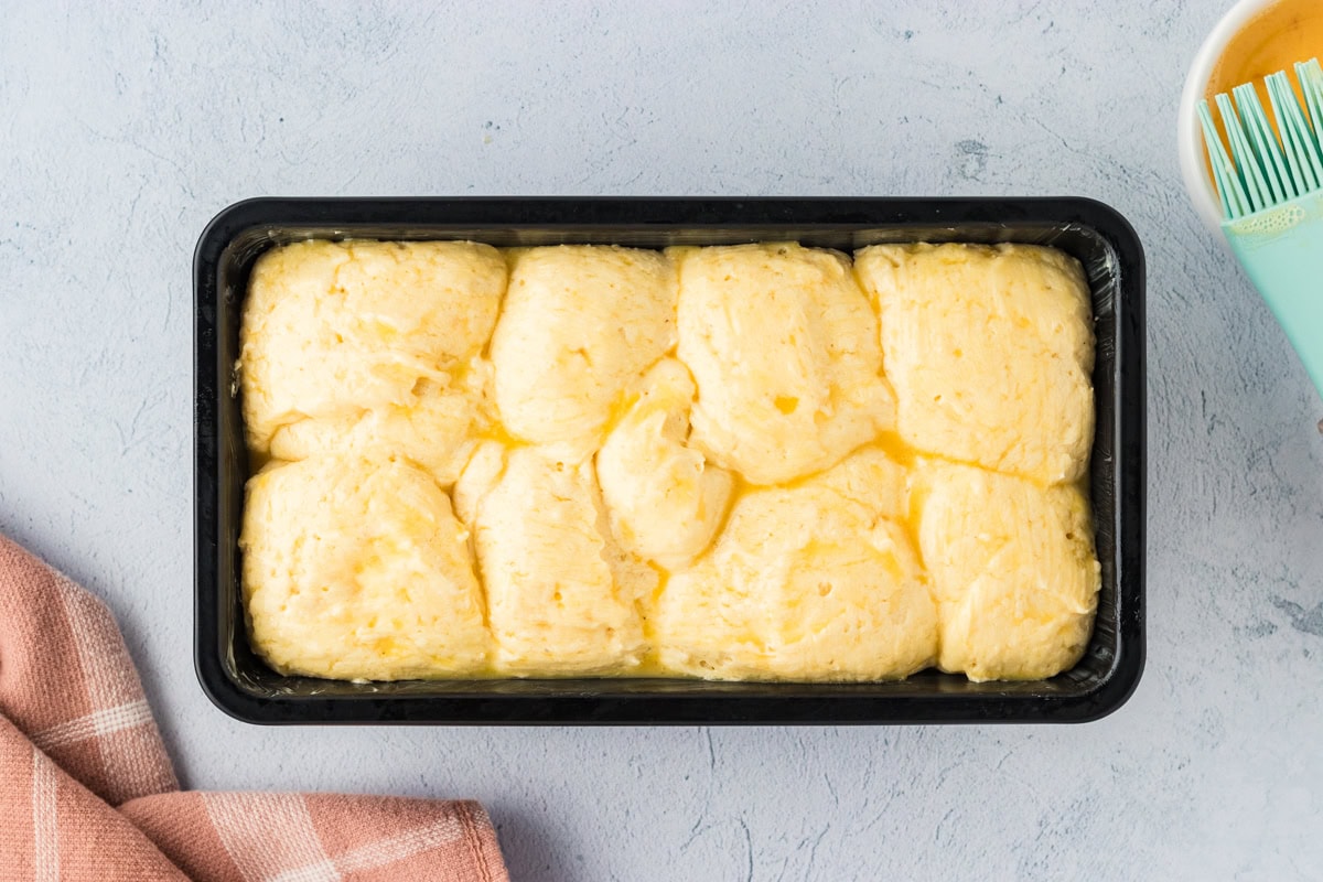 Gluten-free brioche dough brushed with egg wash in a loaf pan.