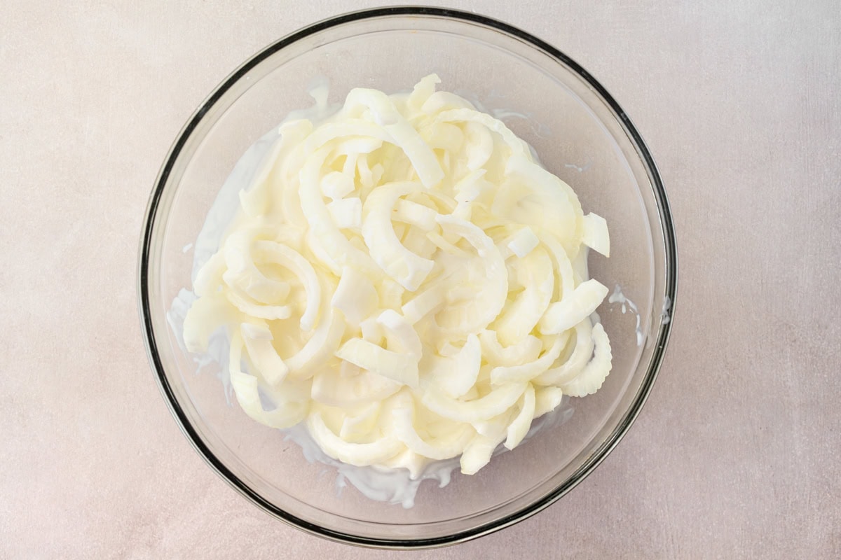 Sliced onions with buttermilk in a mixing bowl.