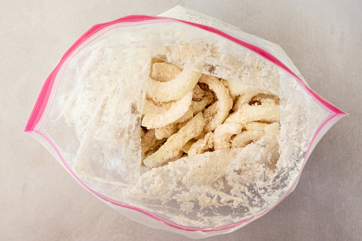 Onion slices tossed in flour and seasonings in a zip top bag.