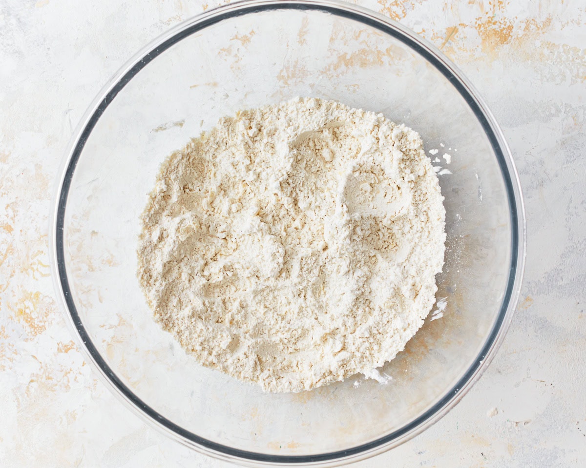 Cold butter cut into the dry ingredients for gluten-free puff pastry in a glass mixing bowl.