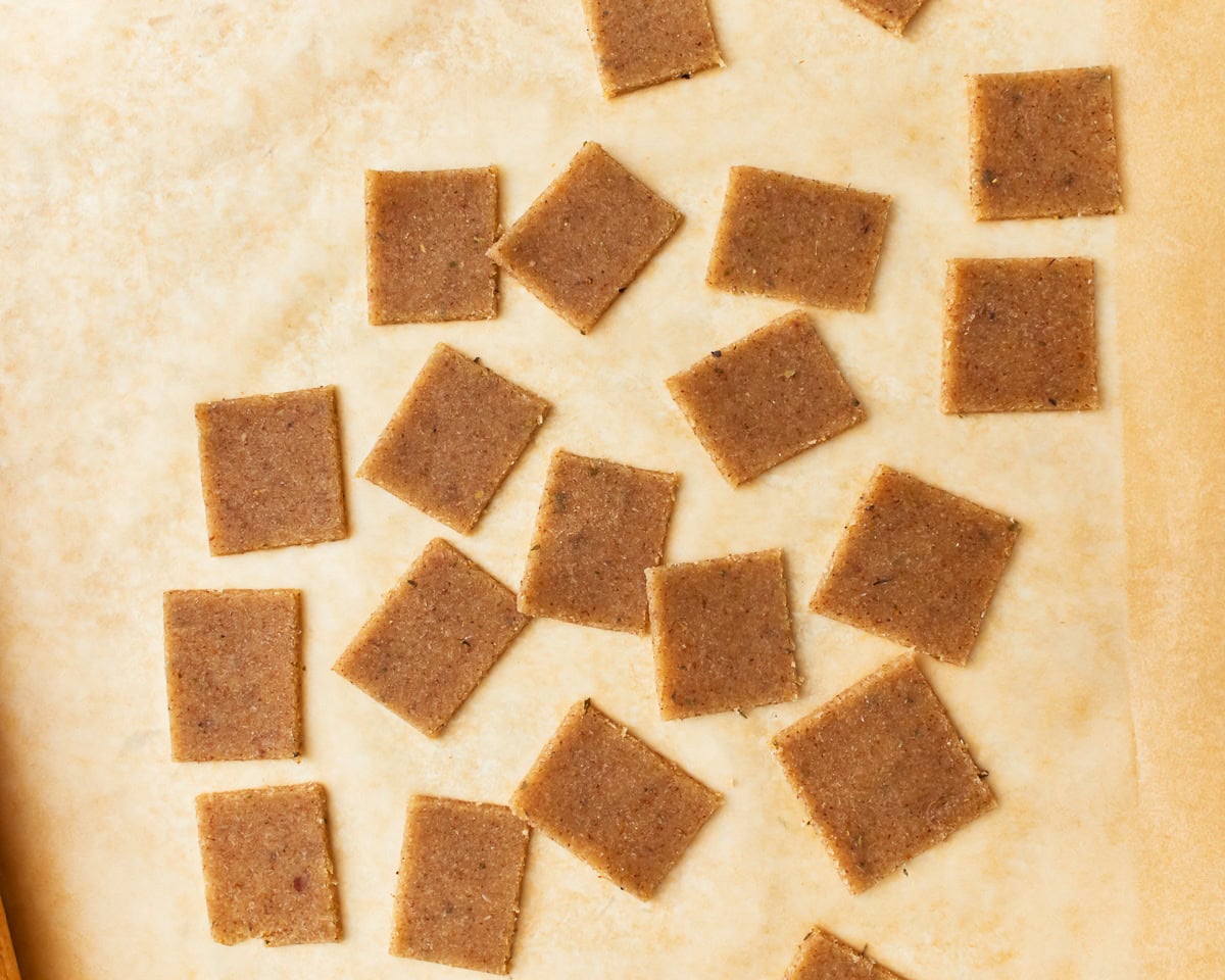 Almond flour cracker dough cut into little rectangles on a parchment lined baking sheet.