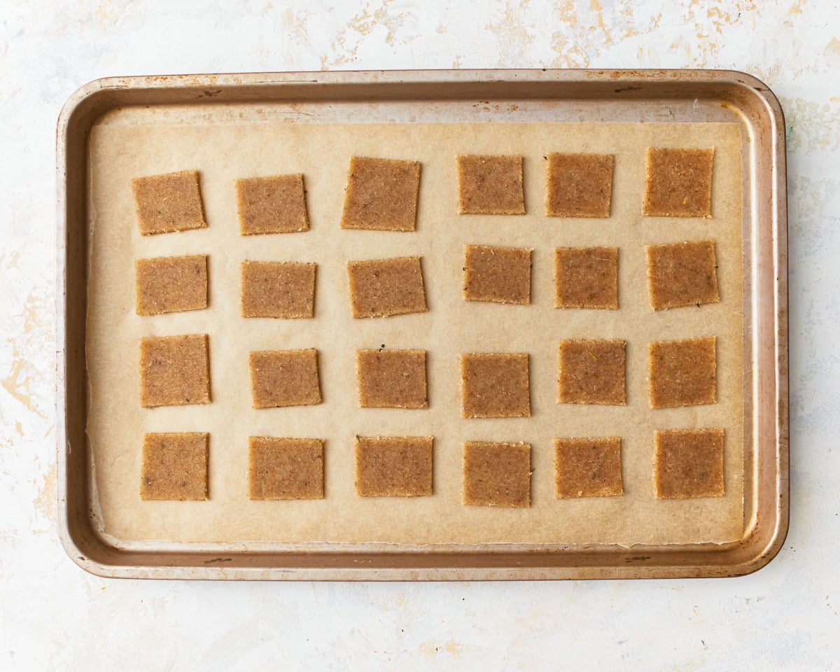 Almond flour cracker dough cut into little rectangles spaced out on a parchment lined baking sheet.