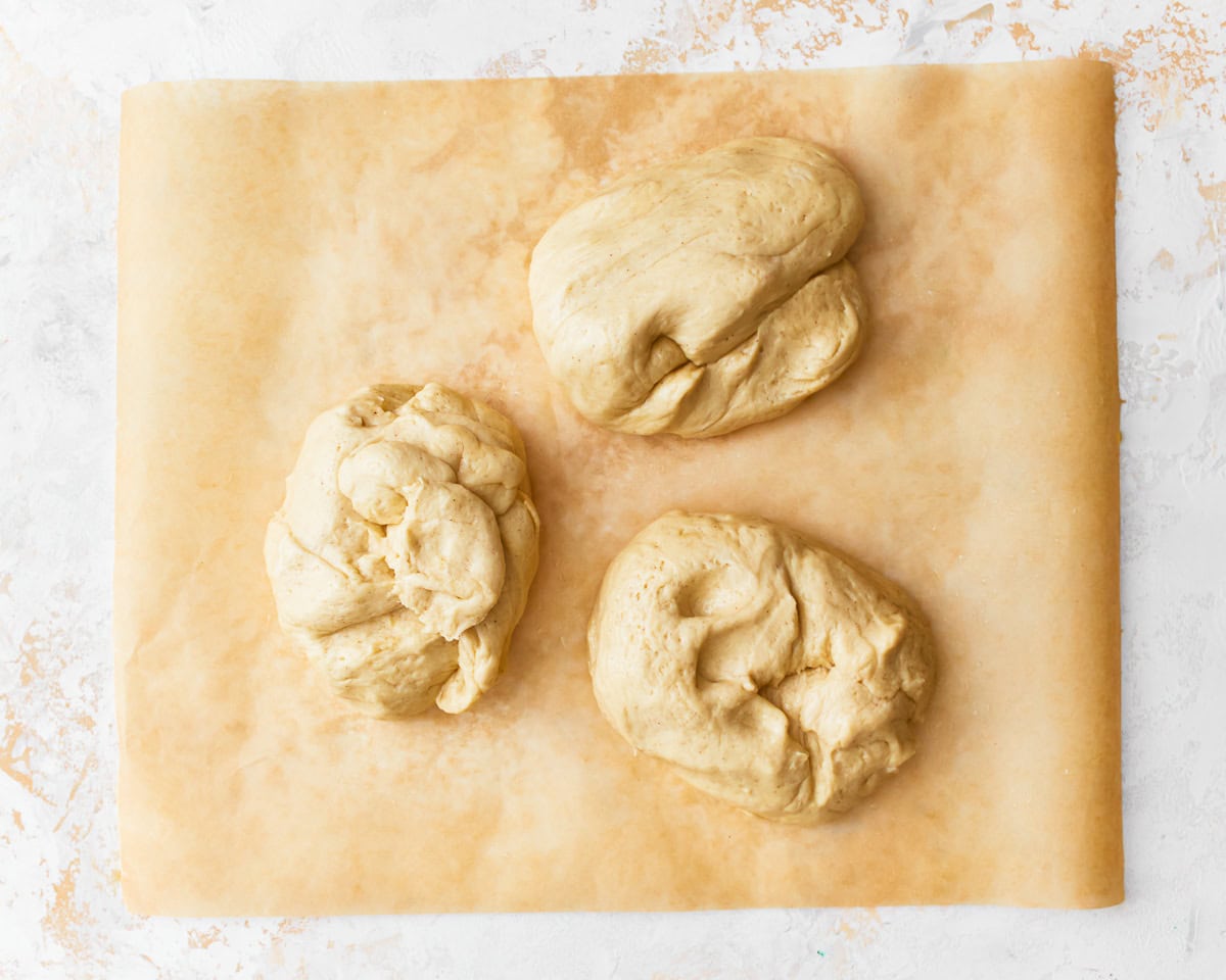 Gluten-free challah bread divided into three portions on a piece of parchment paper.