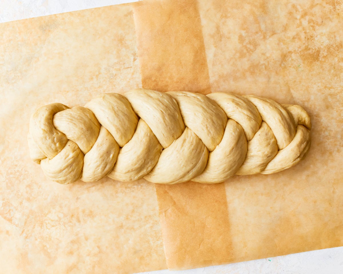 Gluten-free challah bread dough shaped into a braided loaf on a piece of parchment paper.