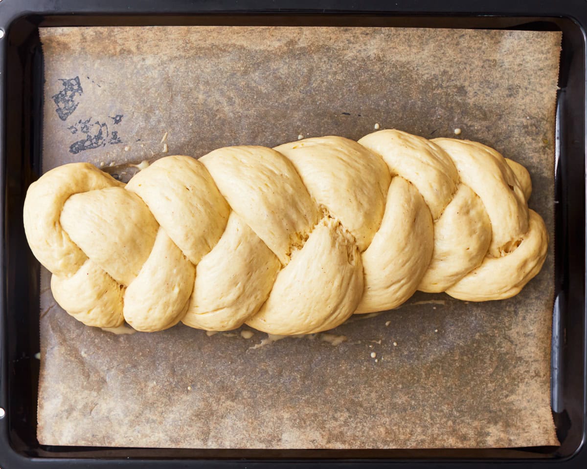 Gluten-free challah bread dough shaped into a braided loaf on a parchment lined baking sheet.