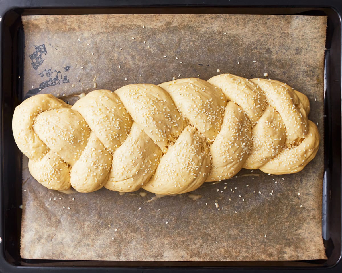 Gluten-free challah bread dough shaped into a braided loaf and topped with sesame seeds.